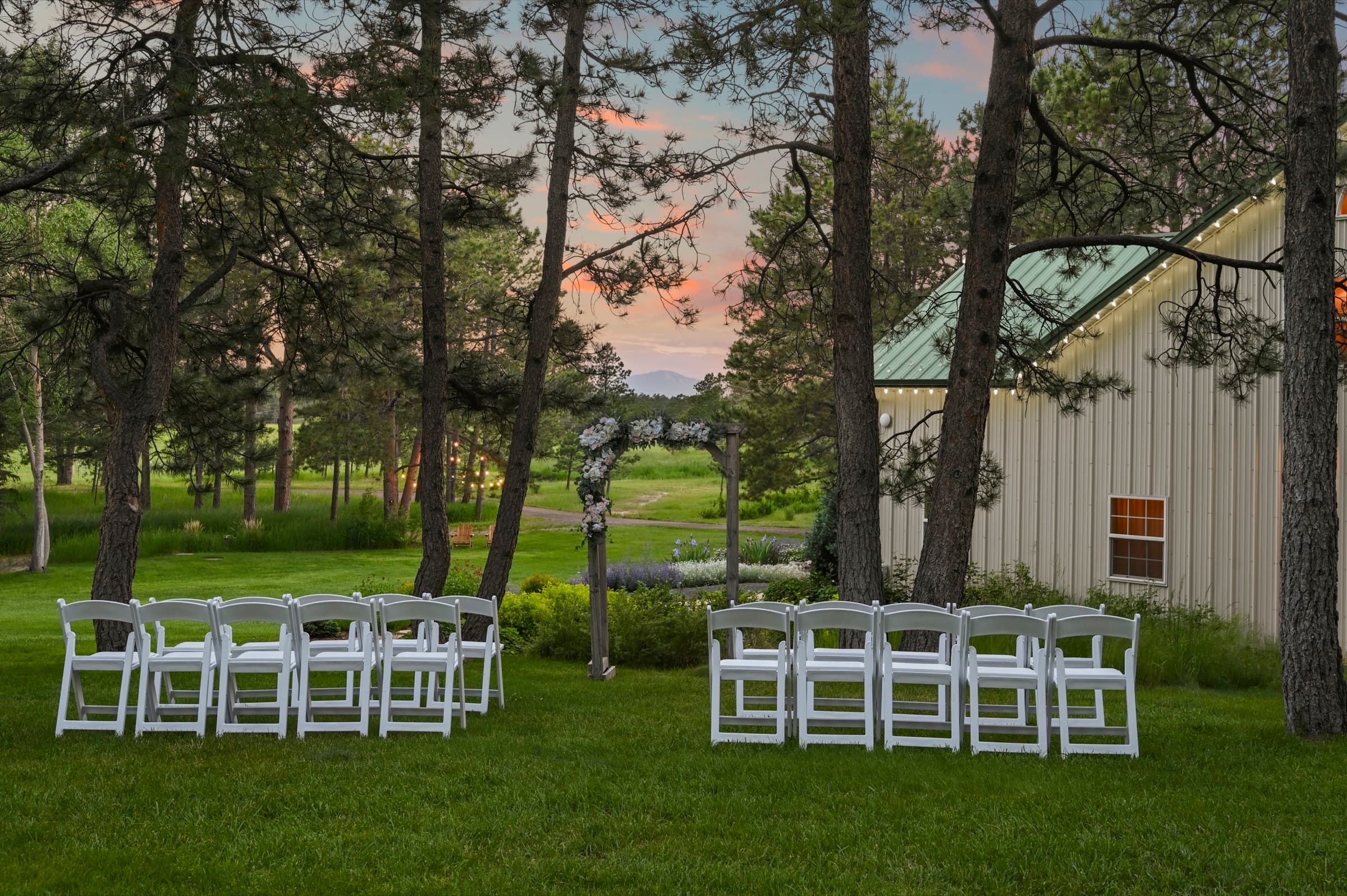 Outdoor wedding ceremony set with white chairs and a floral arch at dusk at Black Forest Meadows in Black Forest, Colorado