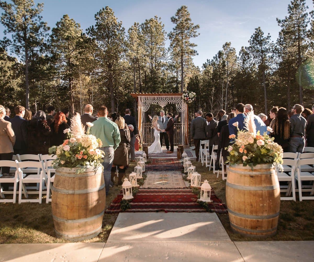 Outdoor wedding ceremony with wine-barrel florals and guests among the pines at Wedgewood Black Forest in Black Forest, Colorado