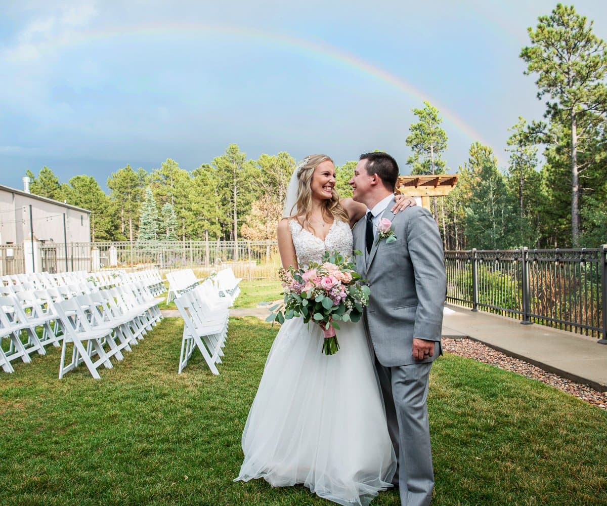 Newlyweds with a rainbow arcing over the ceremony lawn at Wedgewood Black Forest in Black Forest, Colorado