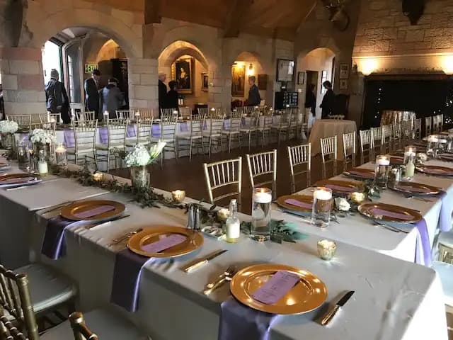 Castle banquet hall set for a wedding reception with gold chargers and stone archways at Cherokee Ranch & Castle in Sedalia, Colorado
