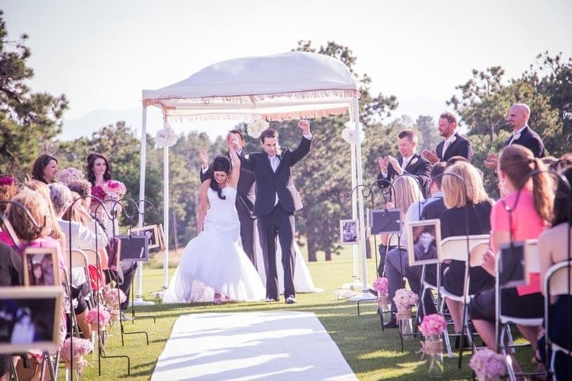 Newlyweds celebrating their recessional under a chuppah on the golf course with mountain views at The Country Club at Woodmoor in Monument, Colorado