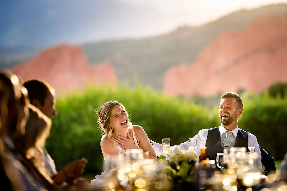 Bride and groom laughing at their outdoor reception with the red rock formations behind them at Garden of the Gods Resort in Colorado Springs