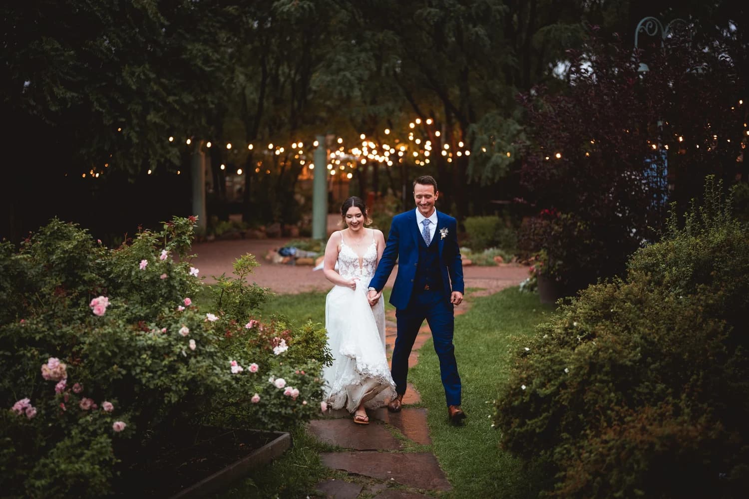 Couple walking a garden path strung with cafe lights at Hillside Gardens & Event Center near Monument, Colorado