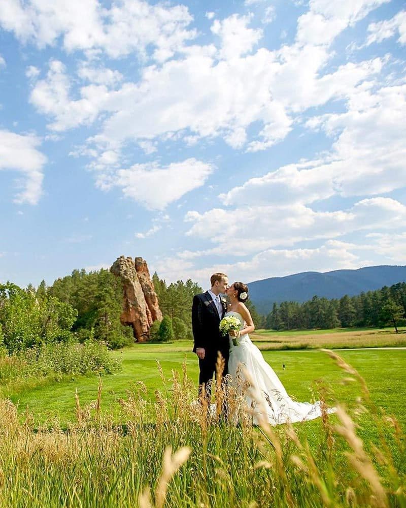 Bride and groom kissing in a meadow with a red rock spire and mountains behind them at Perry Park Country Club in Larkspur, Colorado