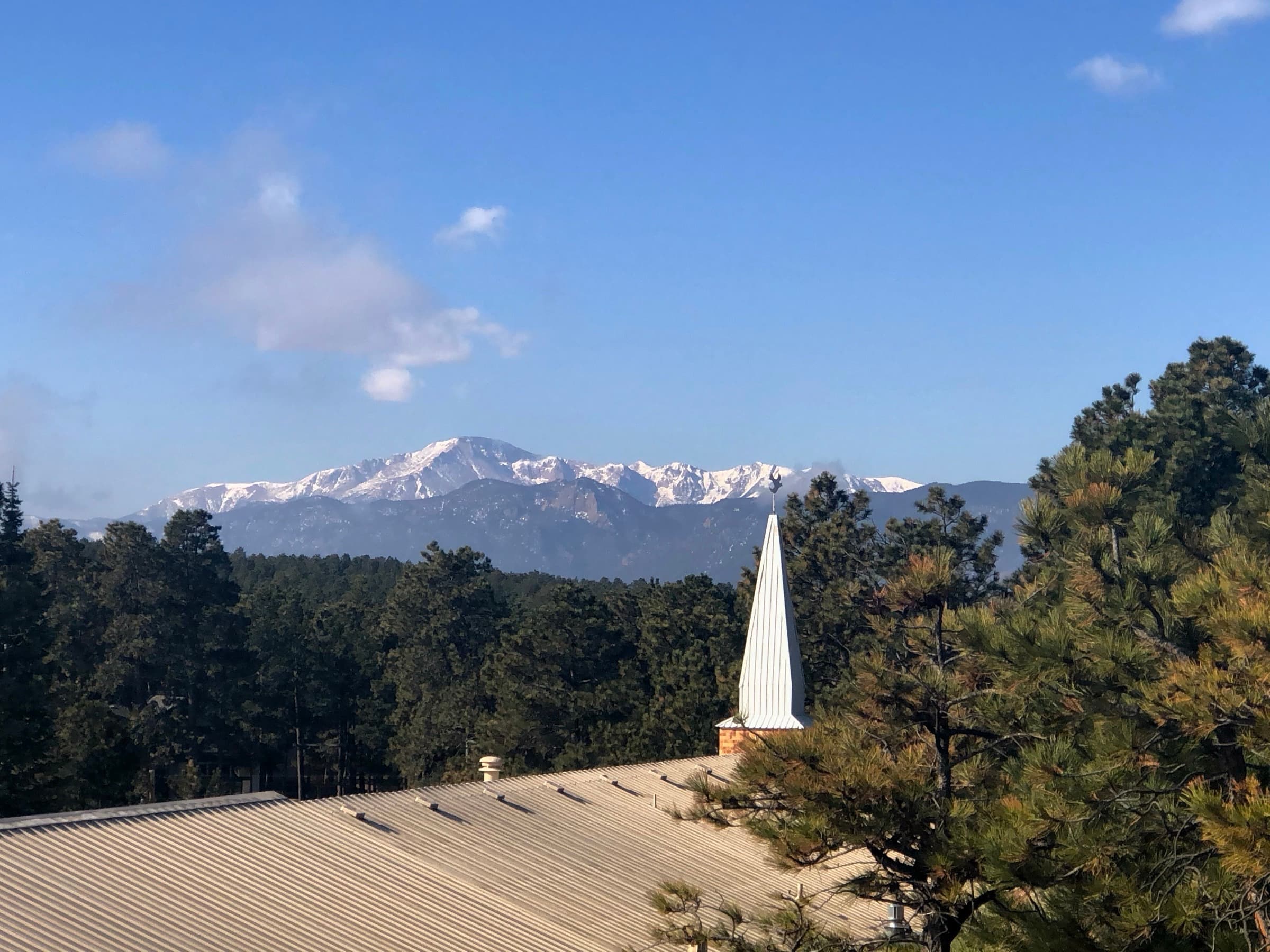 Snow-capped Pikes Peak rising behind the white steeple of The Church at Woodmoor in Monument, Colorado
