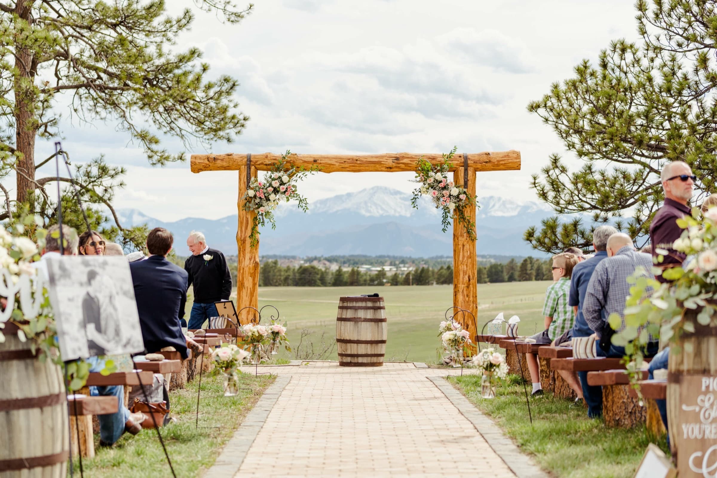 Outdoor wedding ceremony under a rustic wooden arch with Pikes Peak in the distance at Younger Ranch in Monument, Colorado